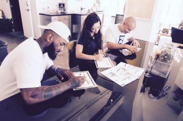Rapper The Game, left, and Darice Smolenski, center, sign paperwork making The Game co-owner of The Reserve medical marijuana dispensary in Santa Ana.
